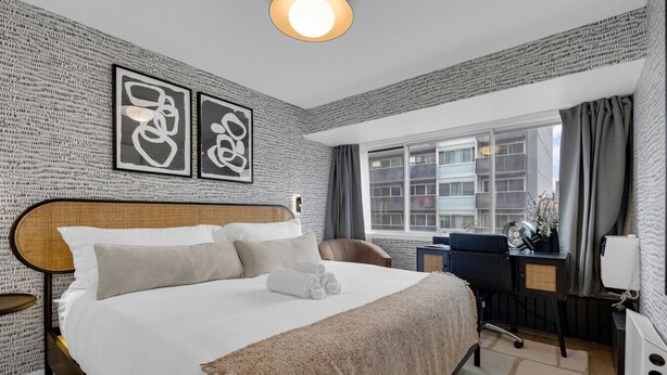 Ein Hotelzimmer mit einem großen Bett, einem Schreibtisch mit Stuhl, einem Fenster mit Vorhängen und Bildern an der Wand.