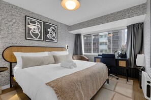 Ein Hotelzimmer mit einem großen Bett, einem Schreibtisch mit Stuhl, einem Fenster mit Vorhängen und Bildern an der Wand.