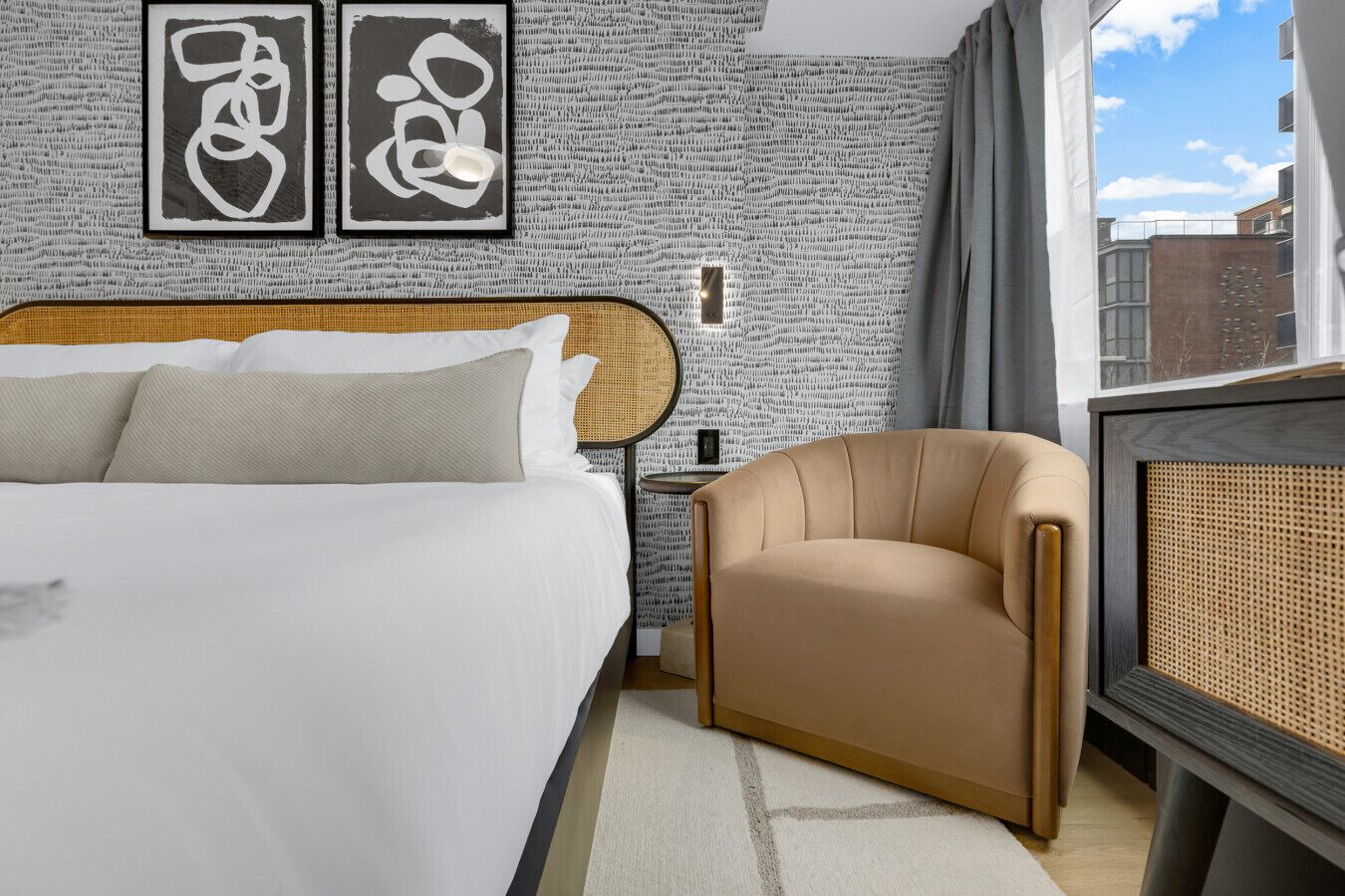 Habitación de hotel con una cama grande, una silla, una mesita y una pared decorada con arte abstracto.
