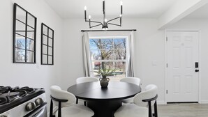 Comedor con mesa redonda, seis sillas, lámpara de araña, estufa y ventana con cortinas.