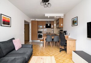 Ein modernes Wohnzimmer mit grauem Sofa, einem Holzespeisetisch und einer Küche im Hintergrund.