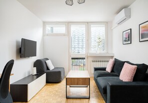 Un salon moderne avec un canapé, une table basse, un téléviseur et une fenêtre donnant sur la ville.