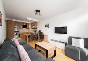 Ein modernes Wohnzimmer mit einer Couch, einem Couchtisch, einem Fernseher und einer Küchenzeile mit Holzschränken sowie einem Esstisch.