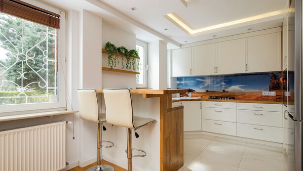 Een moderne keuken met witte kasten, een houten eiland en een barkruk.