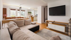 Een moderne woonkamer met een bank, televisie en een eethoek op de achtergrond.