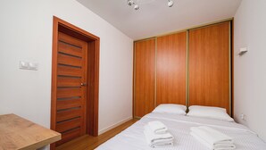 Een slaapkamer met een houten deur, een bed met wit beddengoed en een klein tafeltje.