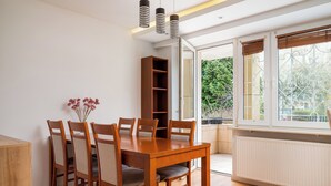 Een eethoek met een houten tafel en stoelen, een boekenkast en een raam met uitzicht op groen.