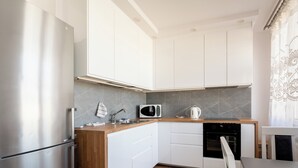 Una cucina moderna con mobili bianchi, un frigorifero in acciaio inossidabile, un forno a microonde e un bollitore.