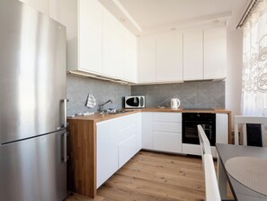 Una cocina moderna con armarios blancos, un refrigerador de acero inoxidable, un microondas y una tetera.