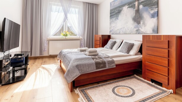 Una camera da letto con un letto, una TV, una finestra con tende, un lampadario e un quadro raffigurante una nave in mare.