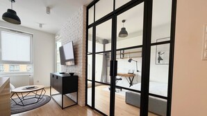 A modern room with a large sliding glass door, a TV on a black cabinet, a desk with a chair, and a bed with a grey mattress. - Street Art Loft Apartment (Wrocław)