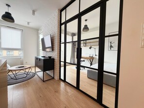 A modern room with a large sliding glass door, a TV on a black cabinet, a desk with a chair, and a bed with a grey mattress. - Street Art Loft Apartment (Wrocław)