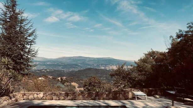 Piscina con pared de piedra y sillas de descanso, rodeada de árboles y con vista a montañas distantes.