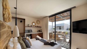 Una habitación de hotel moderna con cama, televisor, kitchenette y balcón con mobiliario de exterior.
