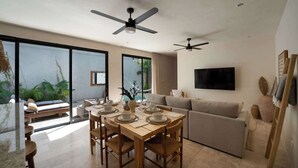 Uma sala de estar moderna com área de jantar, janelas amplas, ventiladores de teto e uma TV de tela plana.