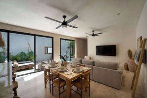 Ein modernes Wohnzimmer mit Essbereich, großen Fenstern, Deckenventilatoren und einem Flachbildfernseher.