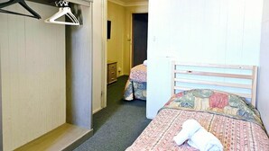 Een hotelkamer met een bed, een garderobe, een spiegel en een deur naar een andere kamer.