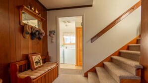 Un intérieur en bois comprenant un banc, un escalier et une porte-fenêtre donnant sur une buanderie.