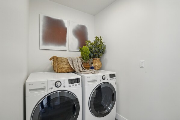 Two front-loading washing machines stacked against a wall with two abstract paintings above them and a potted plant on top. - Designer South Bay Patio Cinema • Near Beach, SoFi (Hawthorne)