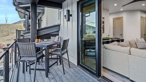 A deck with a table and chairs, a sliding glass door leading to a living area with a sofa and a ceiling fan. - Abode at Canyons Retreat, hot tub, 4 king suites (Park City)