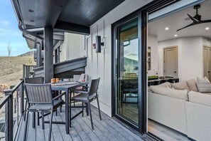 A deck with a table and chairs, a sliding glass door leading to a living area with a sofa and a ceiling fan. - Abode at Canyons Retreat, hot tub, 4 king suites (Park City)