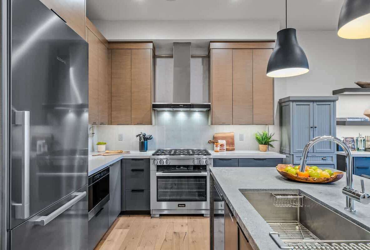 Een moderne keuken met roestvrijstalen apparatuur, houten kasten en een centraal kookeiland met spoelbak en fruitschaal.