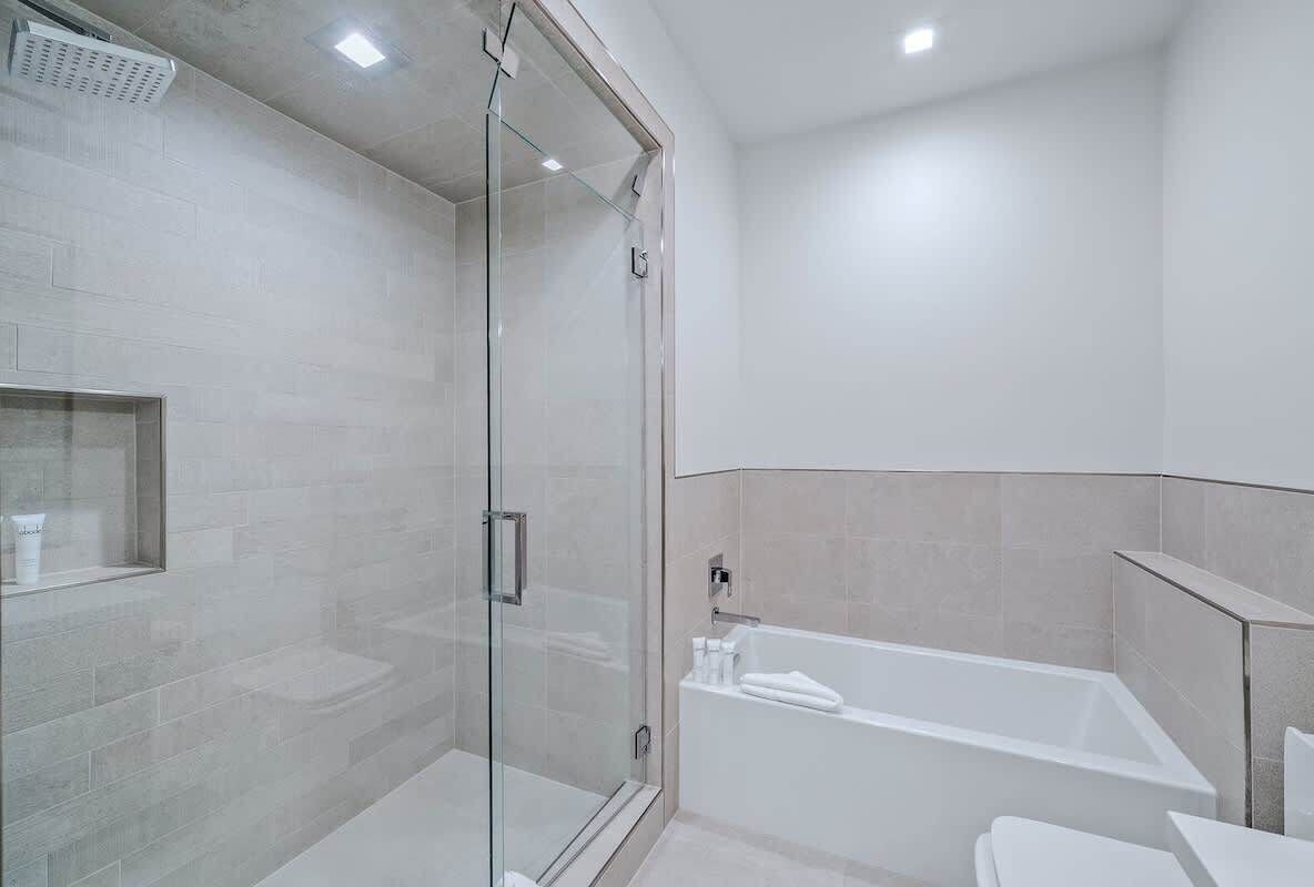 A modern bathroom with a glass shower enclosure, a white bathtub, and a toilet.