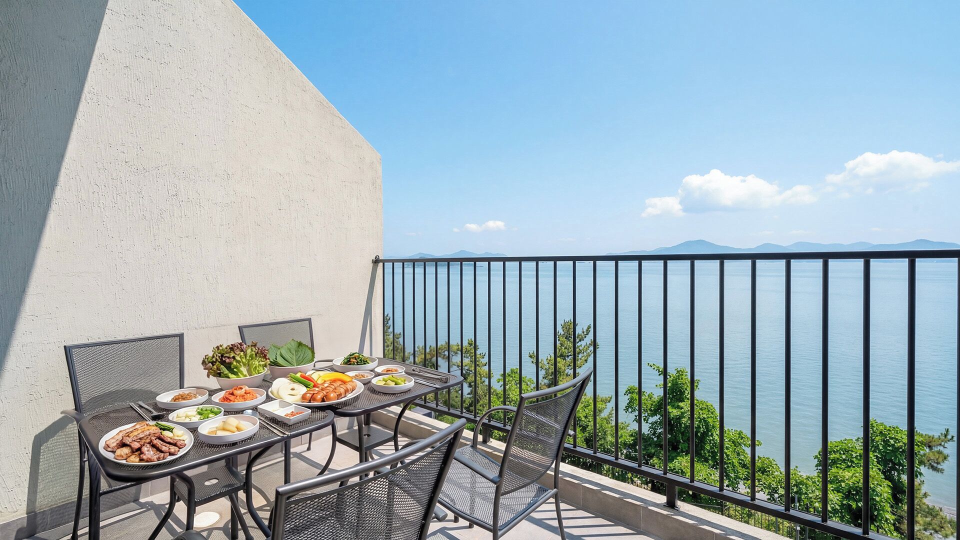 Un balcon avec une table dressée pour un repas, donnant sur une étendue d’eau et sur des montagnes lointaines.