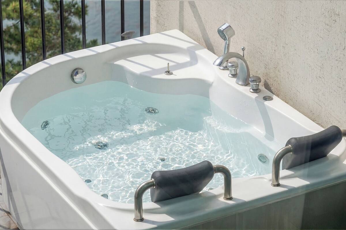 A hot tub with two armrests, a built-in faucet, and a showerhead.