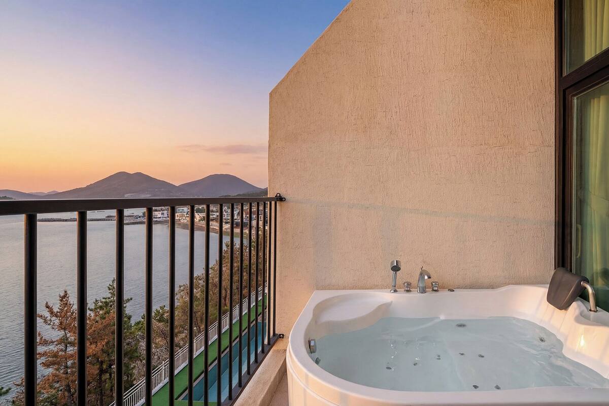 A balcony with a hot tub, a view of a body of water, and a mountain range in the background.