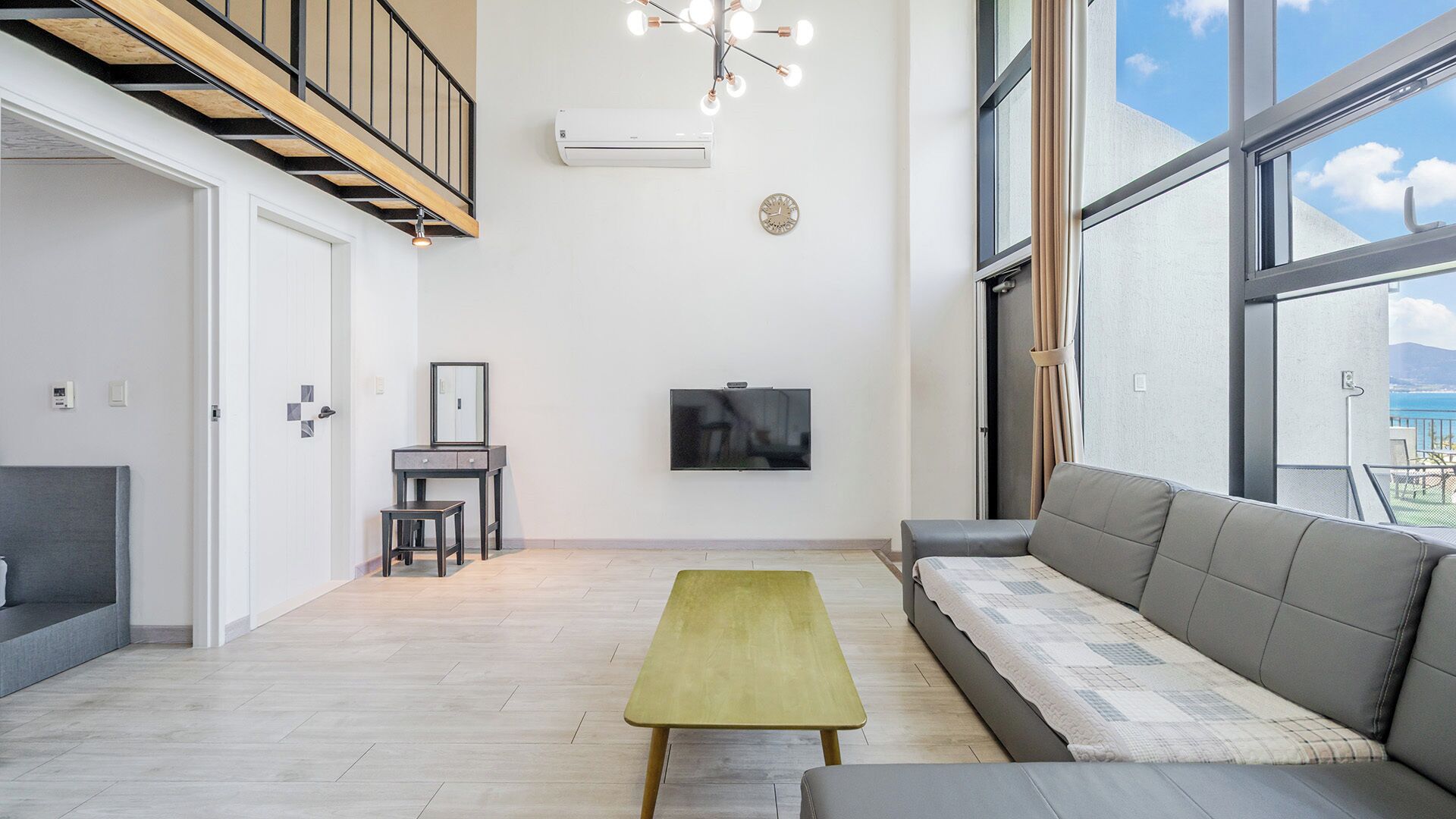 A modern living room with a sofa, a small table, a TV, and a staircase.
