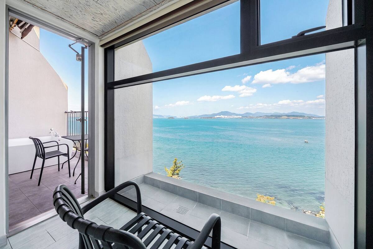 A balcony with a view of the sea, a table, and a chair.