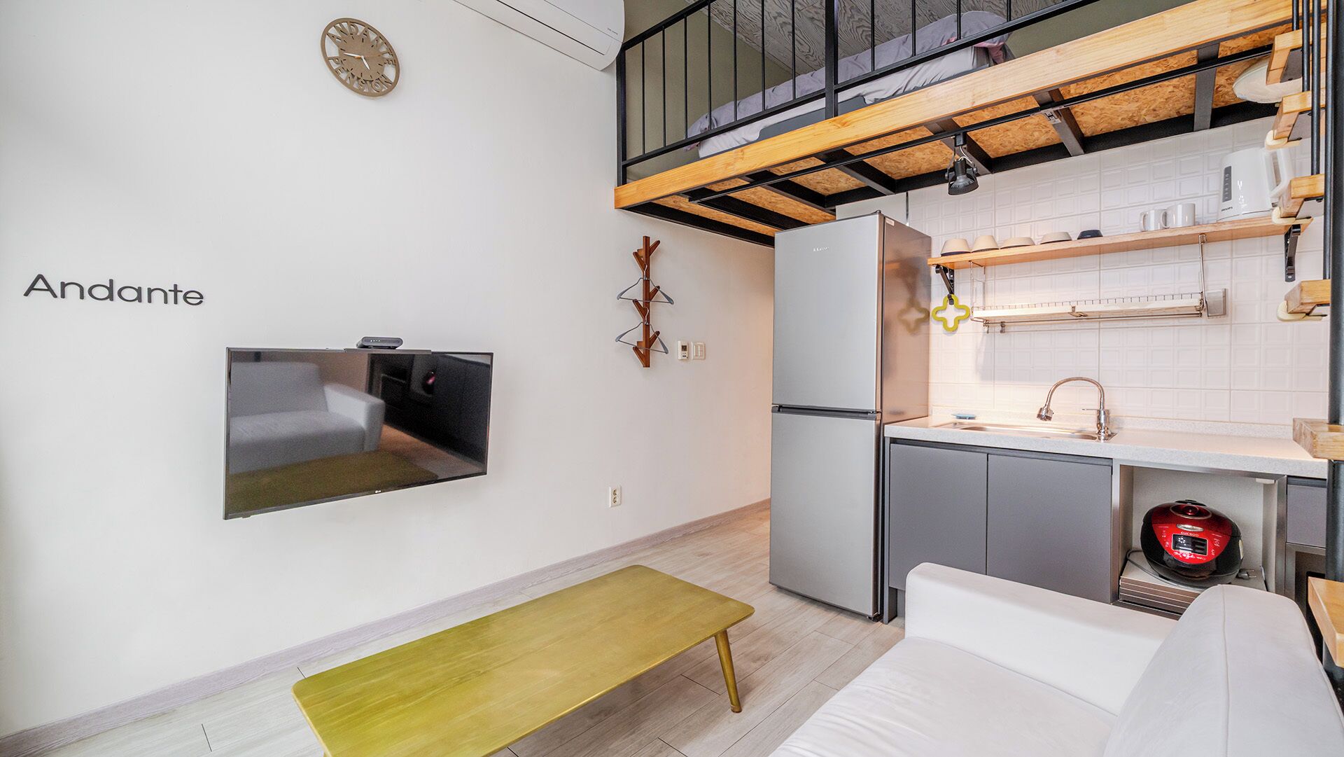 Een compacte keuken met een koelkast, magnetron en spoelbak. In de woonkamer staan een bank en een sofa.