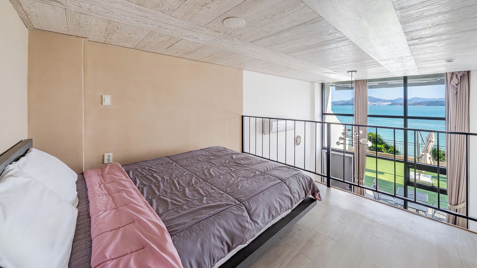 Une chambre avec un lit, une vue sur la mer et un balcon aménagé avec du mobilier d’extérieur.