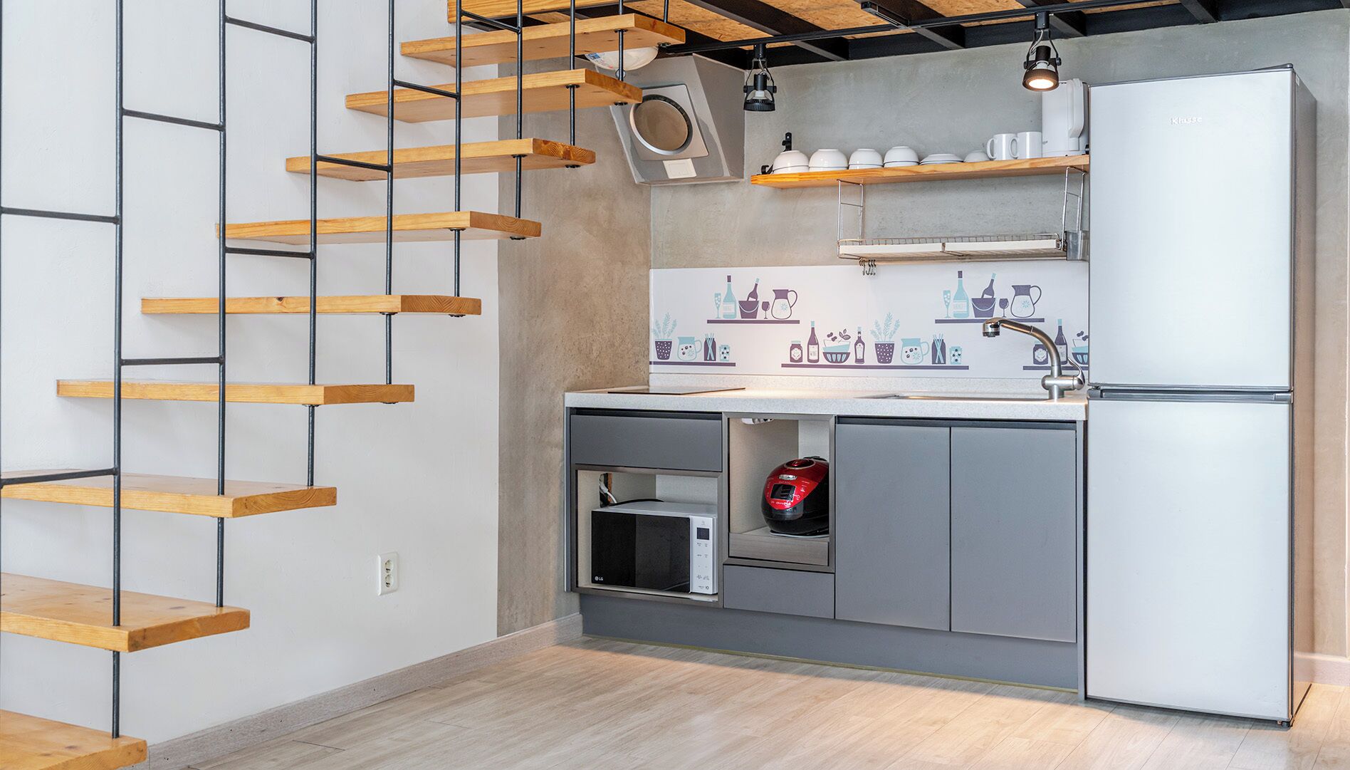 A modern kitchen with a built-in microwave, a refrigerator, and a wooden staircase.
