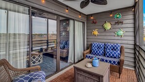 A balcony with wicker furniture, a ceiling fan, and decorative turtle wall art. - Marshside Inn 107 (Murrells Inlet)