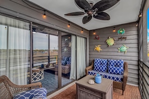 Ein Balkon mit Korbmöbeln, Deckenventilator und Wandkunst mit Schildkrötenmotiven.