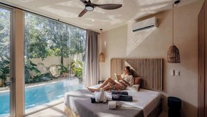 A bedroom with a large bed, a ceiling fan, a bedside table, a hanging light, and a view of a swimming pool. - Villa Selva | 4BR Villa w/ Private Pool & Rooftop (Tulum)