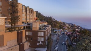 A multi-story hotel with balconies, a parking area, and a view of a hillside town. - Mosaic Mussoorie (Dehradun)