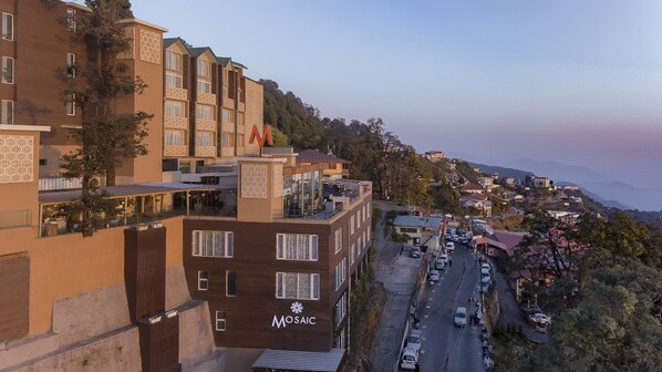 Un hotel de varios pisos con balcones, un estacionamiento y vistas a un pueblo en la ladera.