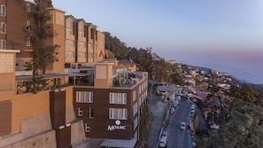 A multi-story hotel with balconies, a parking area, and a view of a hillside town.