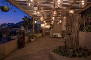 An outdoor terrace with hanging lights, potted plants, and a view of the city at dusk. - Mosaic Mussoorie (Dehradun)