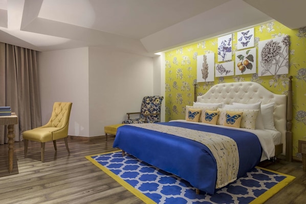 A bedroom with a bed, a chair, a desk, and a wall with floral artwork.