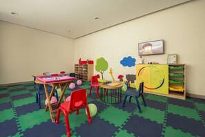 Ein Spielzimmer für Kinder mit Tisch, Stühlen, einem Bücherregal und einer Wand mit Lernmaterialien.