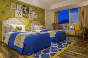 Una habitación de hotel con dos camas, un ventanal grande, una silla y obras de arte en la pared.