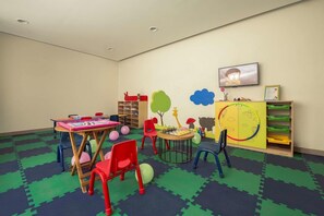 A children's playroom with a table, chairs, a bookshelf, and a wall with educational decorations. - Mosaic Mussoorie (Dehradun)