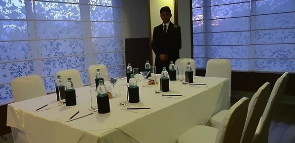 Ein Konferenzraum mit langem Tisch, Stühlen, Wasserflaschen, Gläsern und einem Redner.
