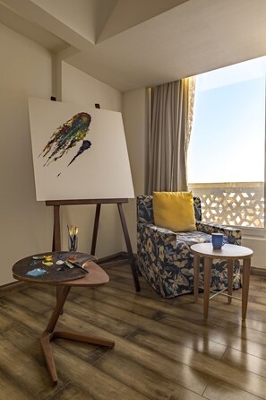 Ein Zimmer mit Holzboden, einem Gemälde auf einem Staffelei, einem blumigen Sofa mit gelbem Kissen und einem kleinen Tisch mit einer blauen Tasse.
