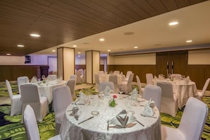 A banquet hall with round tables set for dining, white chairs, and a wooden ceiling.
