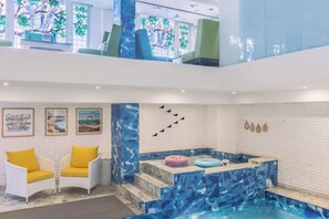 A modern indoor pool area with a mosaic tile design, two white chairs with yellow cushions, and artwork on the walls. - Mosaic Mussoorie (Dehradun)